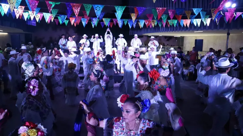 Bailadores de jarana llenan el Palacio de la Música mientras la orquesta toca al fondo, bajo banderines de papel picado