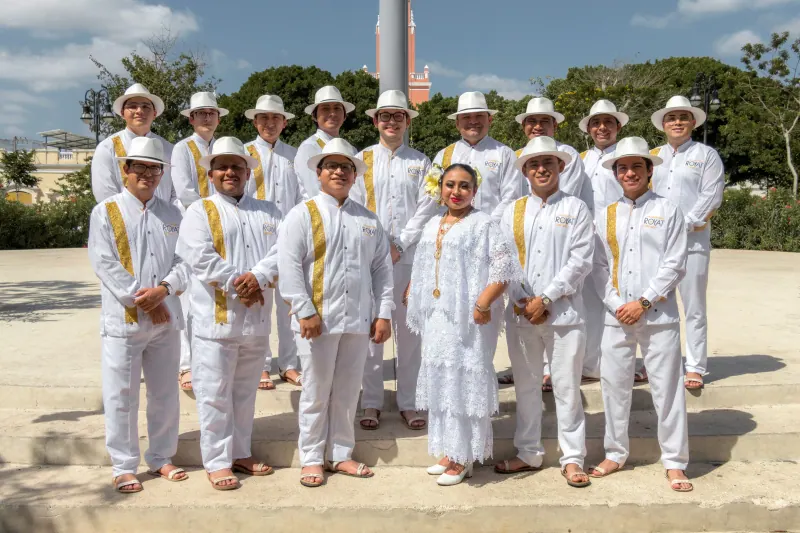 La orquesta completa, vestida de blanco con sombrero, de pie en una plaza arbolada